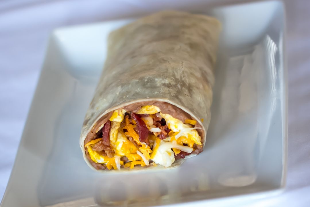 A breakfast burrito cut open, showing scrambled eggs, bacon, melted cheese and refried beans.